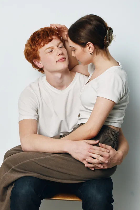 Couple sitting and embracing with affection for love and relationship. Young man and woman in casual wear showing close connection and happiness in studio.