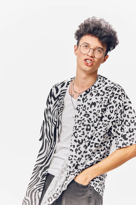 young man wearing stylish animal print shirt, glasses, and white t-shirt posing confidently against plain white background, casual modern fashion look