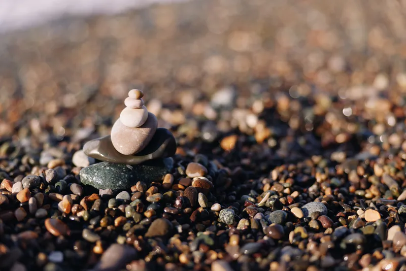 Stone stack on a pebble beach showing balance and calm, with a tiny tower of smooth rocks and sunlight highlighting texture and natural harmony across the shore