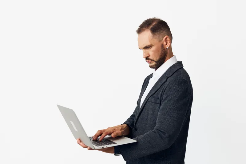 A professional businessman works on a laptop against an isolated colored background, conveying focus, confidence, and calm competence in a corporate setting.