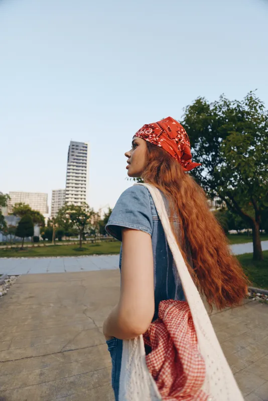 Lifestyle woman in modern boho-western denim street style with red bandana and long hair walking outdoors in film color, urban background, casual and relaxed.