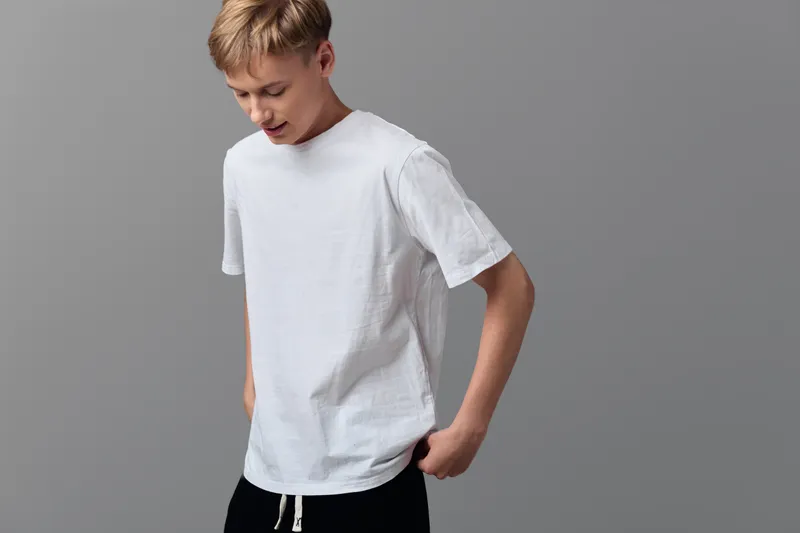 Man in white t shirt standing against a minimalist gray backdrop, casual wear vibe with a relaxed pose, simple studio setup and neutral tones for versatile everyday style