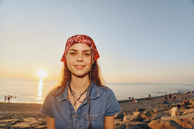 Lifestyle woman in modern boho-western denim street style with a red bandana, warm sunset, and beach background in natural film color tones.