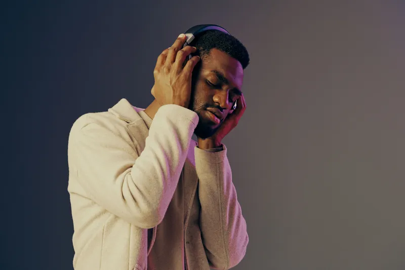 A young Black man enjoying music with headphones, lost in the rhythm, showcasing a relaxed and emotional vibe against a softly lit gradient background