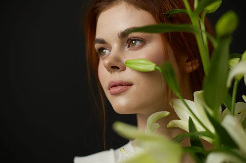 Young woman with fresh flowers, showcasing elegance, natural beauty, and a serene expression against a dark background, emphasizing spring vibes and femininity