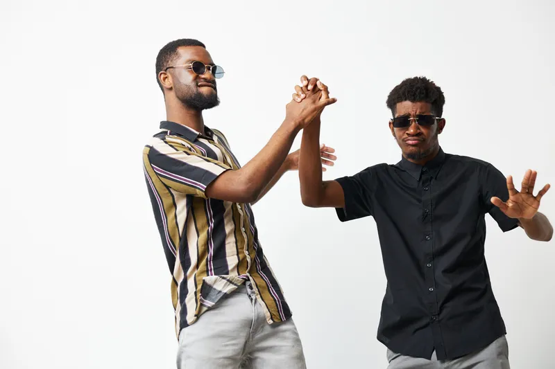 Two African American men joyfully celebrating in stylish outfits, showcasing a fun atmosphere with vibrant energy and playful poses under bright lighting.