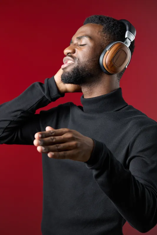 Young African man enjoying music with headphones, wearing a black turtleneck against a red background, expressing joy and relaxation through music