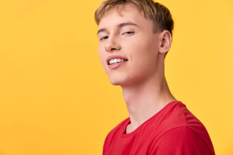 Smiling man in a red shirt stands against a bright yellow background, creating a bold casual scene suitable for lifestyle, fashion, and positive energy themes.