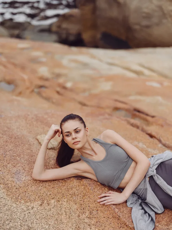 Young woman in activewear resting on rocky terrain, conveying calmness and relaxation in a natural setting with earthy tones and soft lighting