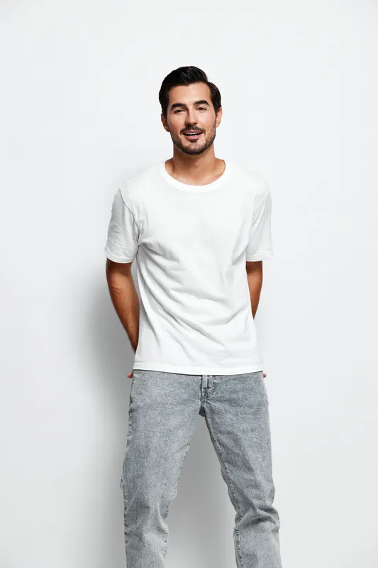 Full body smiling happy cheerful young man wear casual white t-shirt and gray pants look camera stand hands behind back isolated on plain solid light background. Lifestyle concept