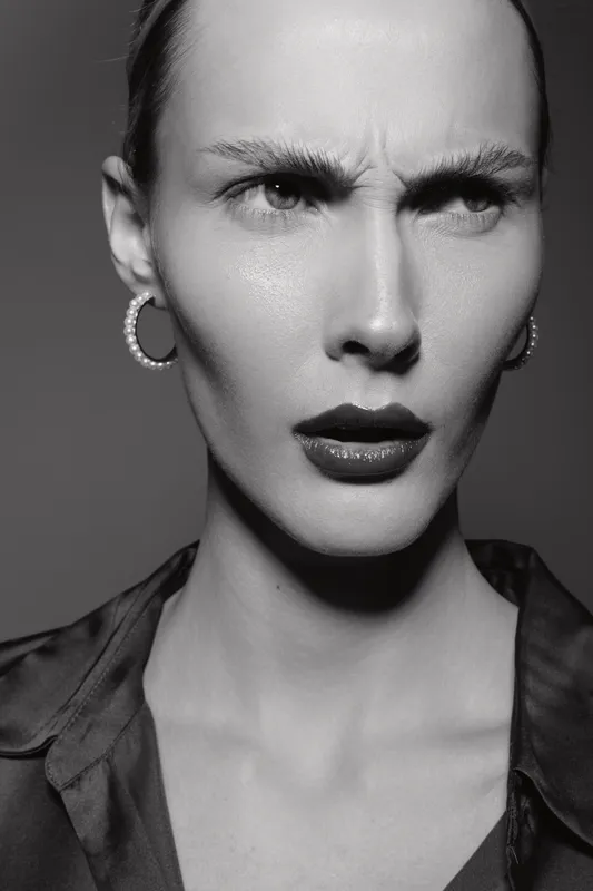 Serious Caucasian woman with pale skin and dark lipstick frowns, showing intense emotion in black and white studio portrait. Concept of mood and facial expression.