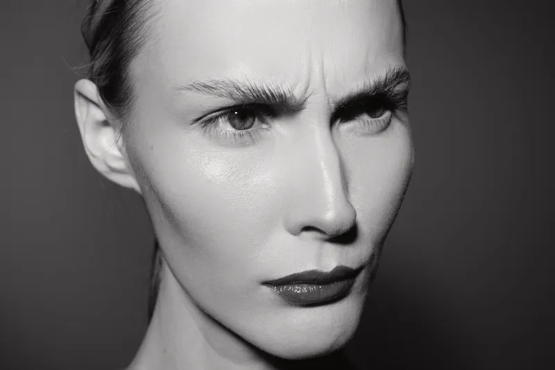 Close-up of a serious young white woman with light skin and furrowed brows. Black and white studio portrait with dramatic lighting highlights facial expression and emotions.