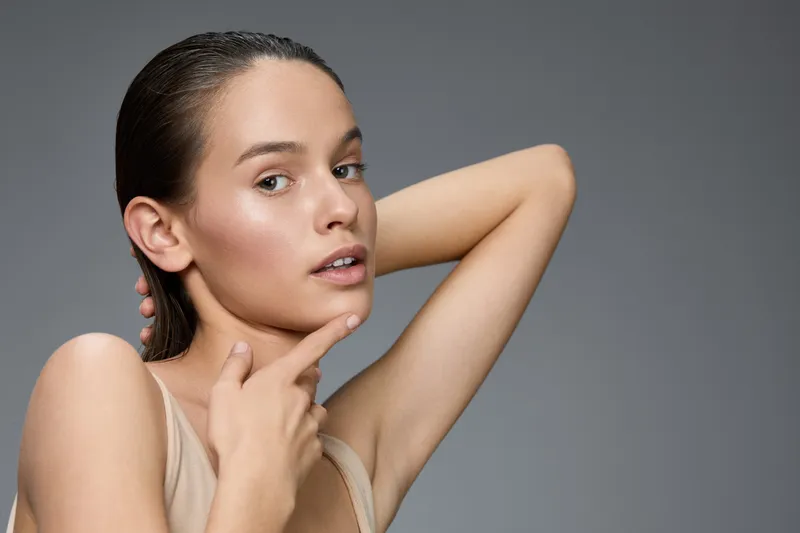 Young woman with flawless skin showcasing natural beauty and confidence against a soft gray background, emphasizing self care and skincare