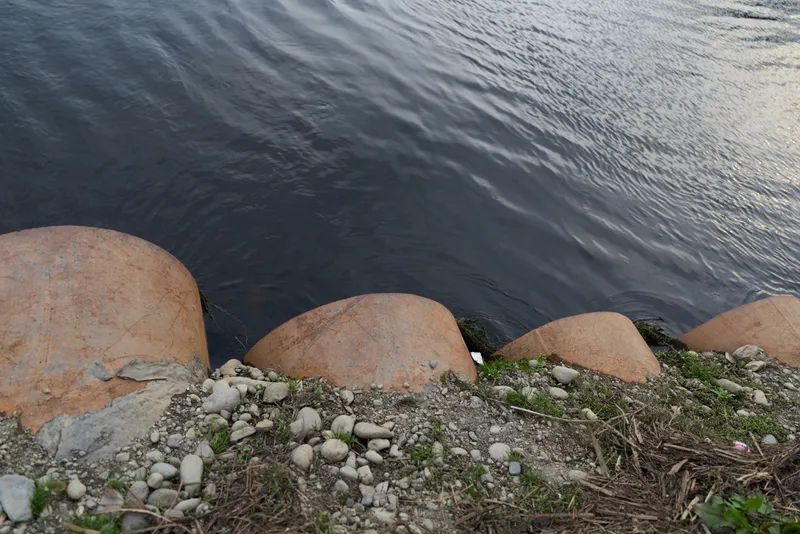 coast shoreline water rocks pebbles nature outdoors landscape calm ripples, stones and boulders by the edge, gravel and sparse grass, tranquil seascape with soft daylight, gentle waves
