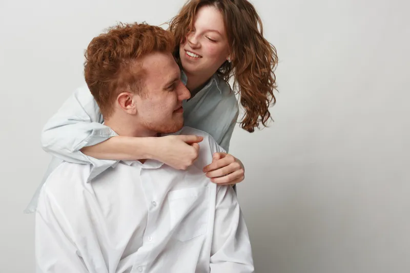 Happy young couple in white shirts embraces and smiles, showing affection and love. Studio portrait with neutral background. Concept of relationships, romance, and intimacy.