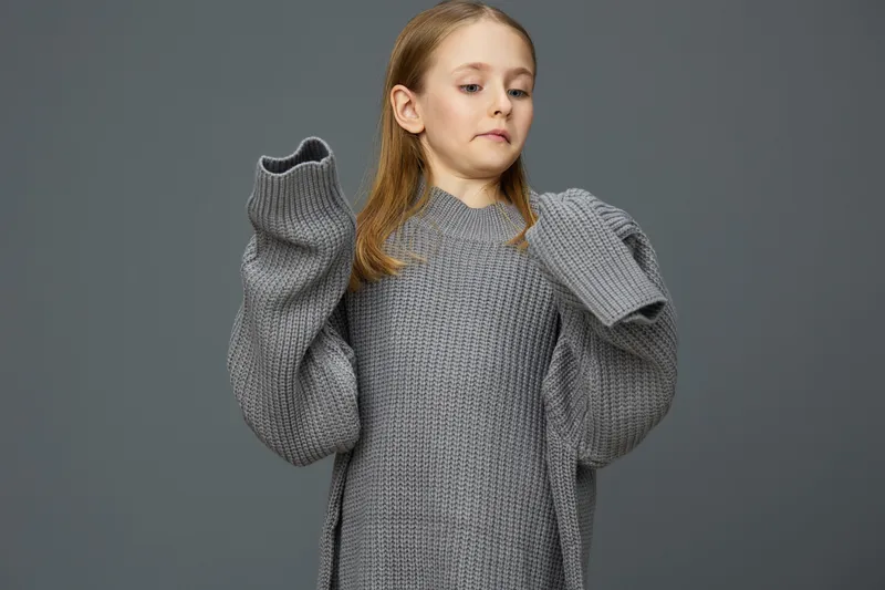 Young girl in oversized gray sweater showcasing confidence and style against a solid gray background, ideal for fashion and lifestyle concepts