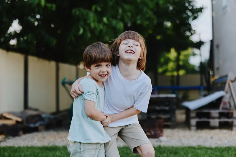 Joyful children playing together outdoors, laughing and sharing a fun moment in a sunny garden setting, surrounded by greenery and a playful atmosphere.