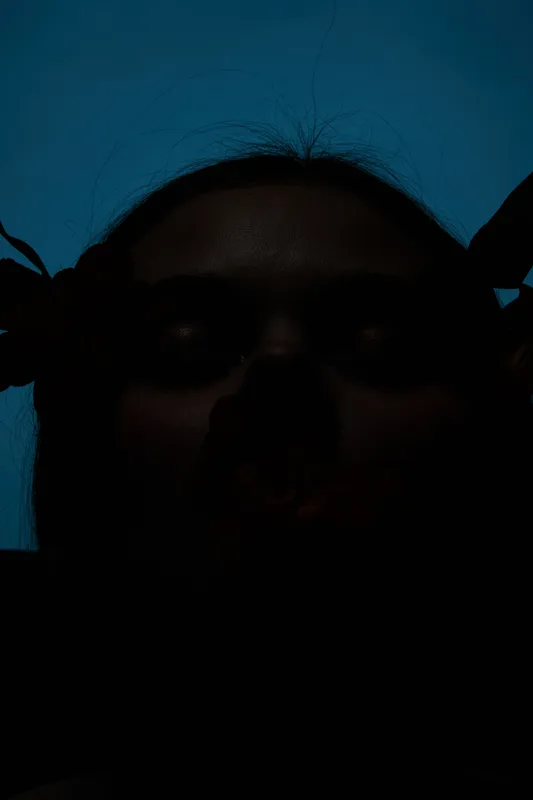 Dark silhouette portrait of a young woman against a blue background, conveying emotions of mystery and introspection with artistic lighting elements