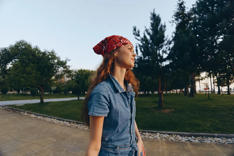 lifestyle woman in modern boho-western denim street style with red bandana, walking outdoors in warm natural light, film color tone enhancing relaxed casual vibe.