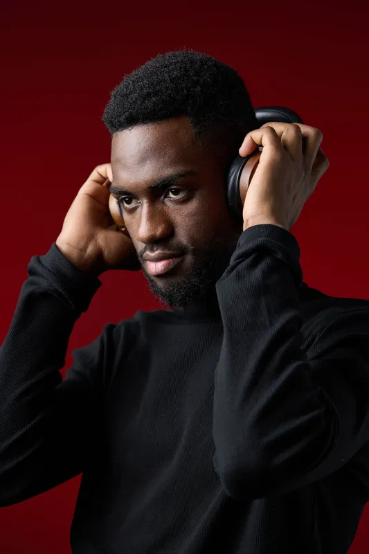 Young Black man wearing headphones, focused on music, against a deep red background, capturing a moment of connection and emotion in music