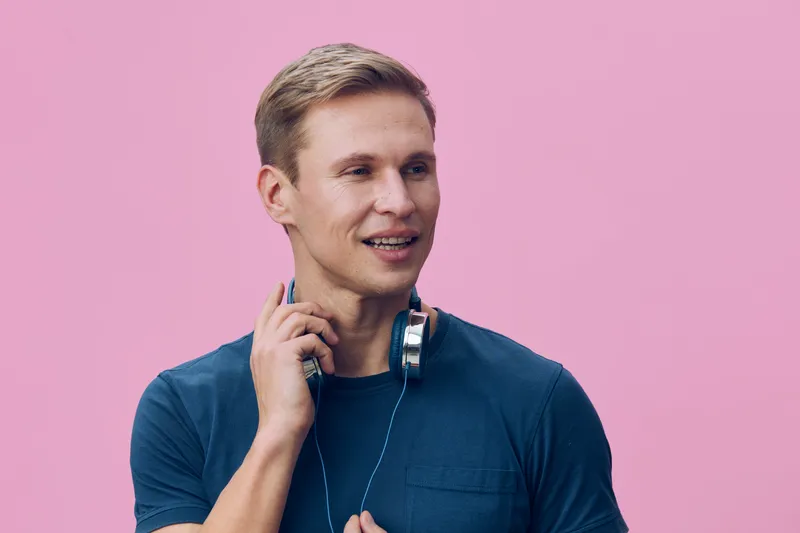 smiling man with headphones casual wear look side hold cord digital nomad lifestyle cybersecurity concept pink background