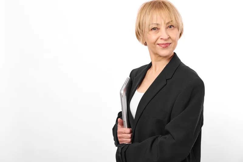 Senior woman in business blazer portrait, smiling on white background, confident office style, short blonde hair, studio lighting, formal workwear, calm professional mood