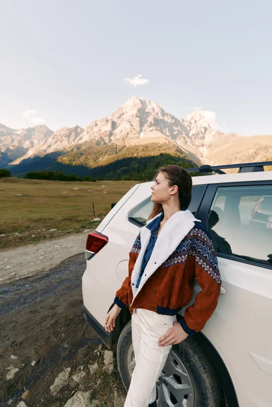 Woman and car in mountains on travel roadtrip, portrait in nature with outdoor adventure vibe, leaning by suv on dirtroad, scenic landscape and relaxed exploration journey.