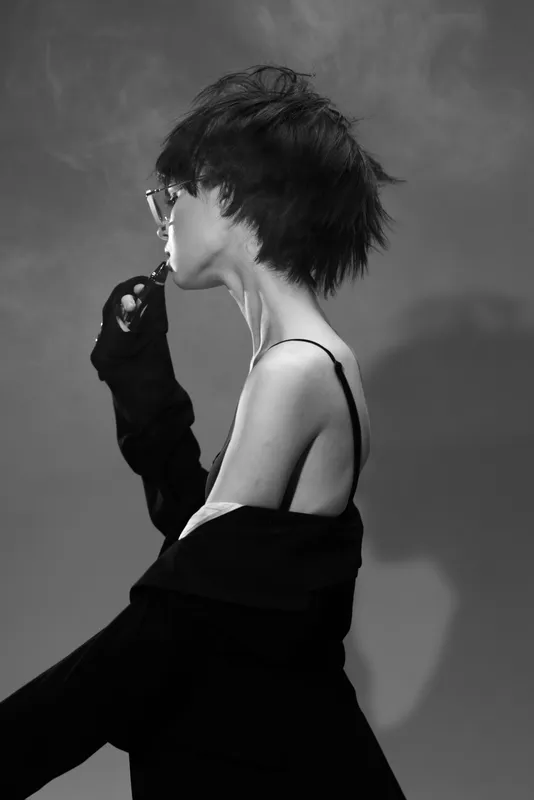 Black and white portrait of a woman smoking with a contemplative mood and stylish short hair in a minimalist setting.