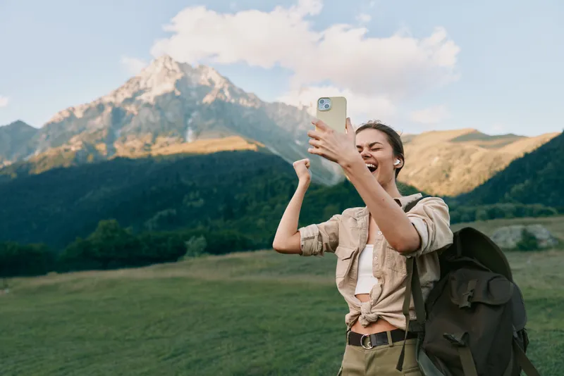 Selfie taking hiker woman with backpack smiles in the mountains during daytime outdoors