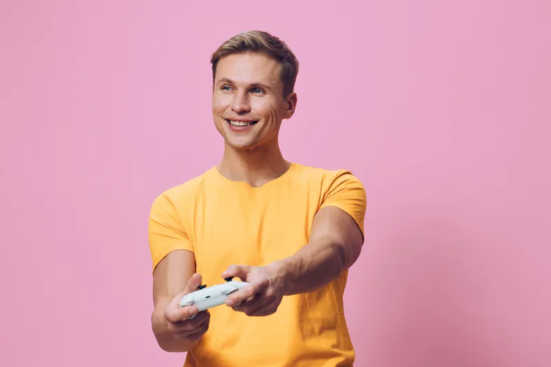 smiling young man play video game hold controller wear yellow t-shirt isolated pink background digital detox entertainment concept