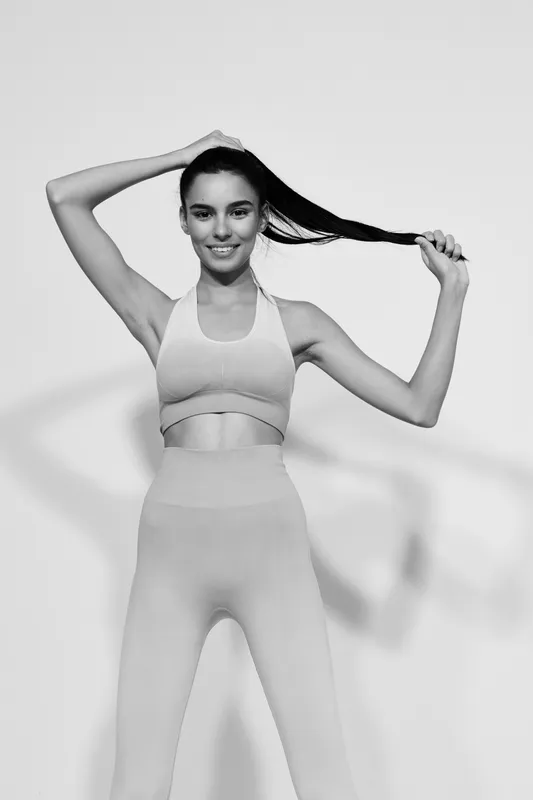 Sport fitness woman in seamless activewear smiling while holding her ponytail, showing strength, health, and energy. Black and white portrait with a clean background.