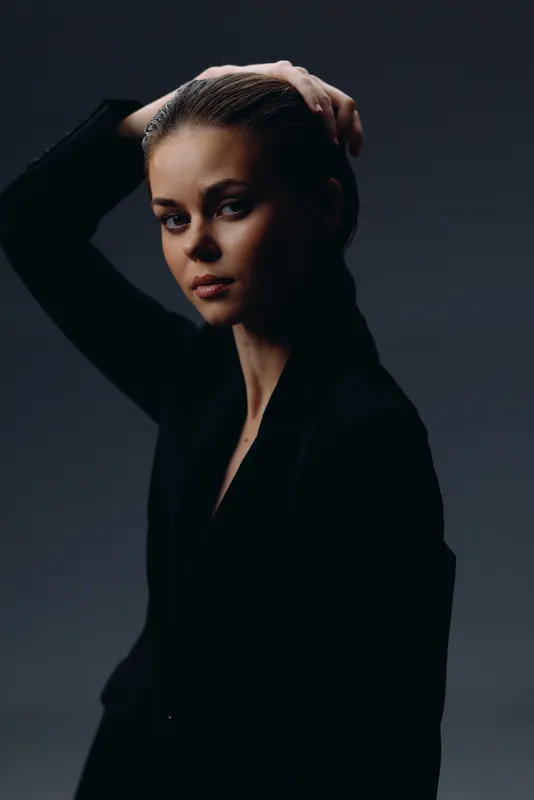 serious woman with hand in hair wearing black jacket in low-key lighting