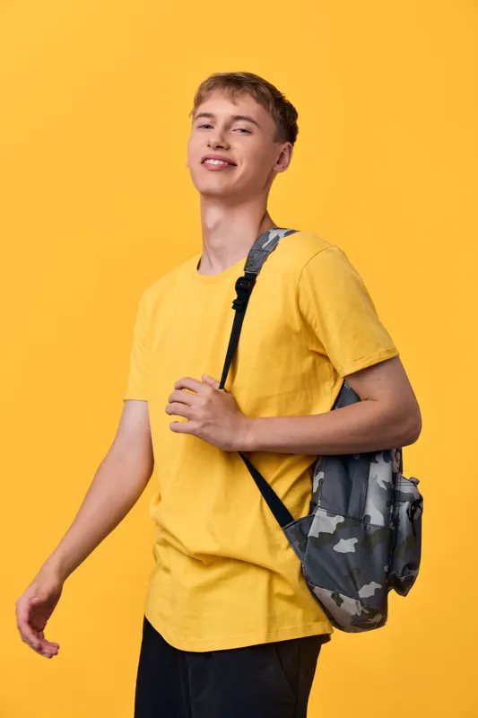 Student with backpack in a yellow tee, posing confidently in a bright studio, showcasing casual fashion and youthful energy for lifestyle and education themed stock image