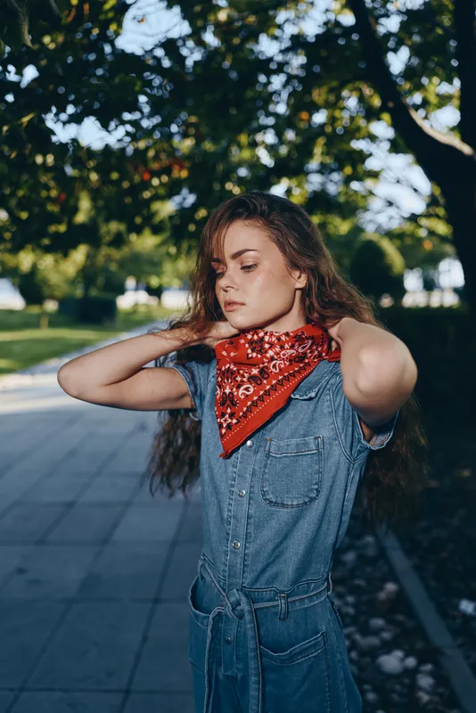 Lifestyle woman in modern boho-western denim street style with a vibrant red bandana, captured with natural light and film color tones, expressing casual cool confidence.