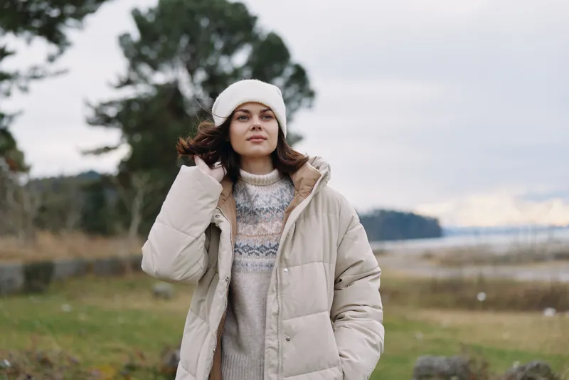 Winter woman outdoor fashion coat portrait in chilly countryside with sweater and beanie, soft light, calm landscape, cozy look for cold weather lifestyle.
