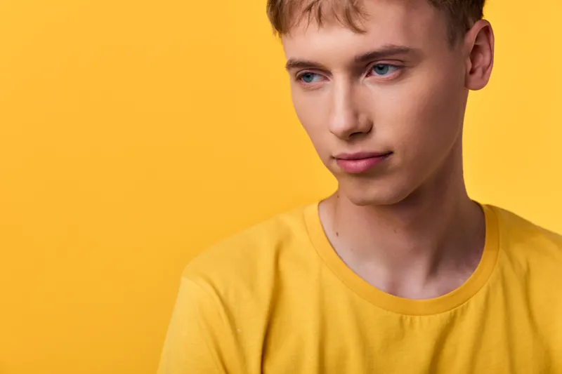 Young man wearing a yellow shirt against a bright yellow backdrop, conveying casual style, quiet contemplation, modern fashion appeal, and clean studio lighting