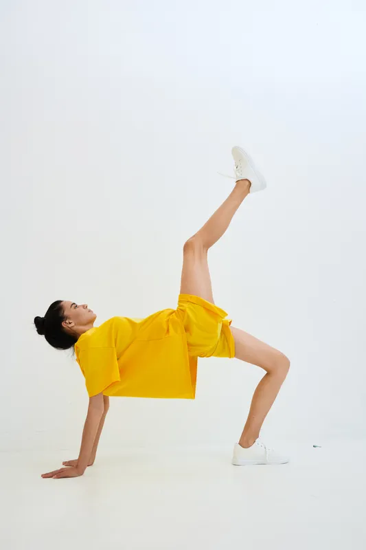 Active woman in yellow sportswear performing modern fitness pose against white background, showcasing flexibility and strength in a minimalist studio setting.