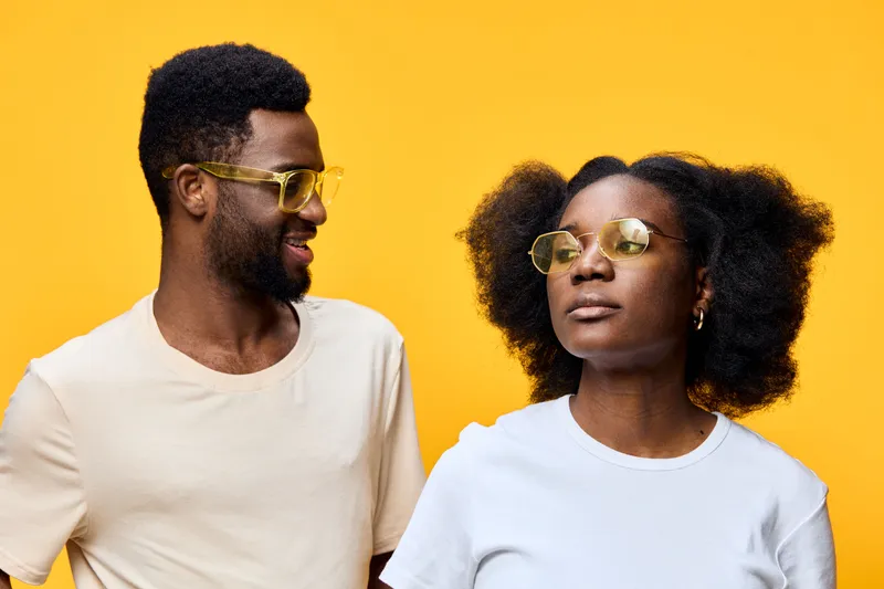 Young diverse couple wearing stylish sunglasses against a vibrant yellow background, exuding confidence and joy, perfect for fashion and lifestyle themes