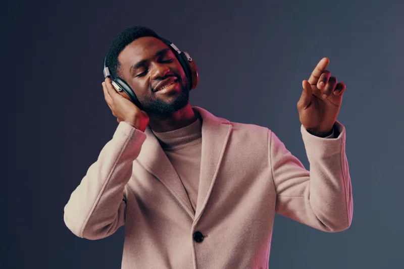 Happy young man enjoying music with headphones, wearing a stylish coat, against a colorful gradient background, embodying joy and relaxation