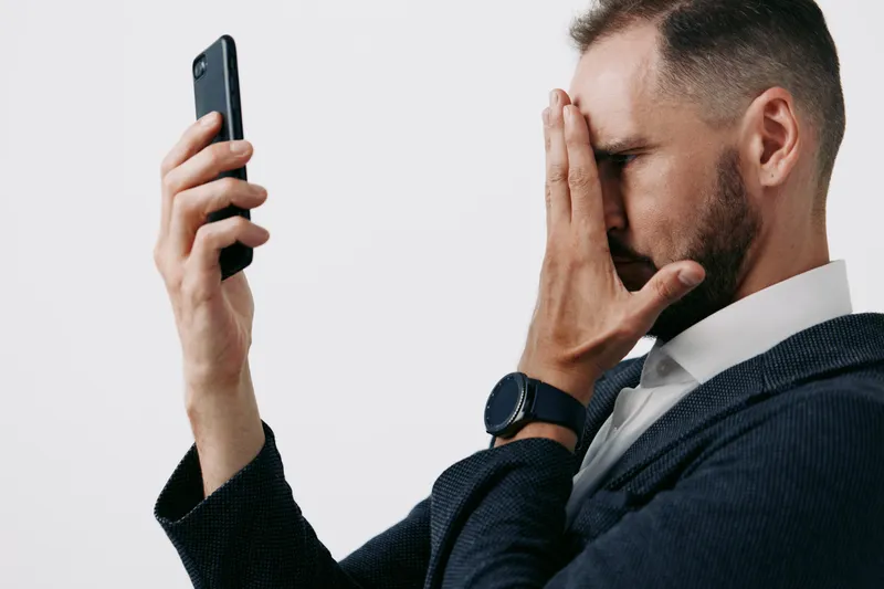 A professional man in a suit, isolated color background, glances at a smartphone with a worried, thoughtful expression, conveying business stress and deep emotion.