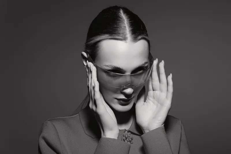 Stylish white woman with pale skin wearing transparent glasses touches her face in monochrome studio portrait. Concept of fashion and elegance.