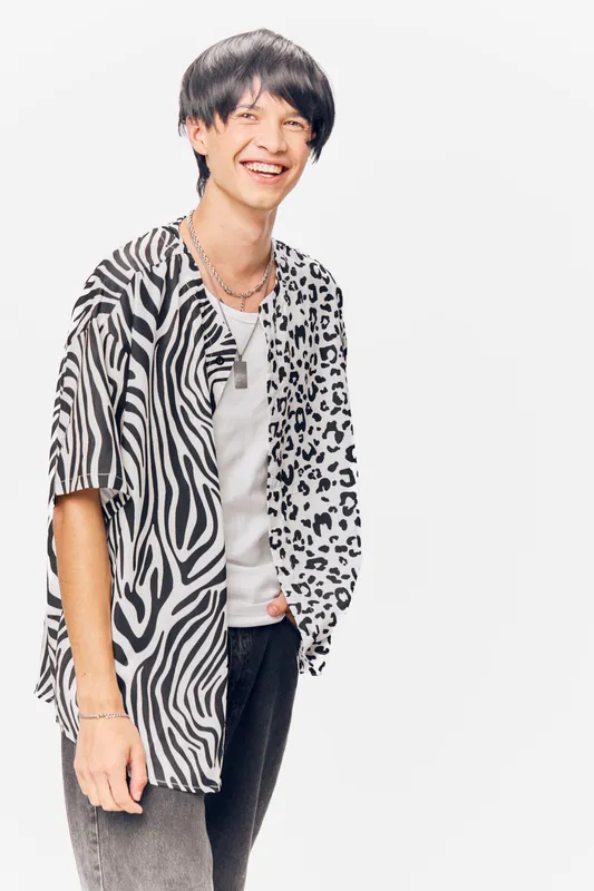 smiling man wearing a black and white patterned shirt with short black hair and casual clothing standing against a plain white background, cheerful and relaxed pose