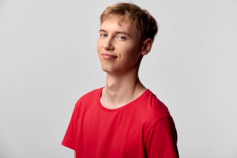 Young man in a red shirt with a smile poses casually in a studio setting, conveying a relaxed mood, modern style, approachable attitude and everyday fashion for lifestyle campaigns
