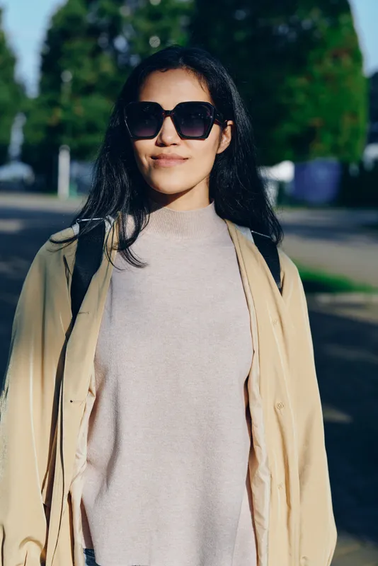 Woman wearing sunglasses, beige trench coat and knit sweater walking outdoors on a sunny day, street fashion scene with confident casual chic vibe