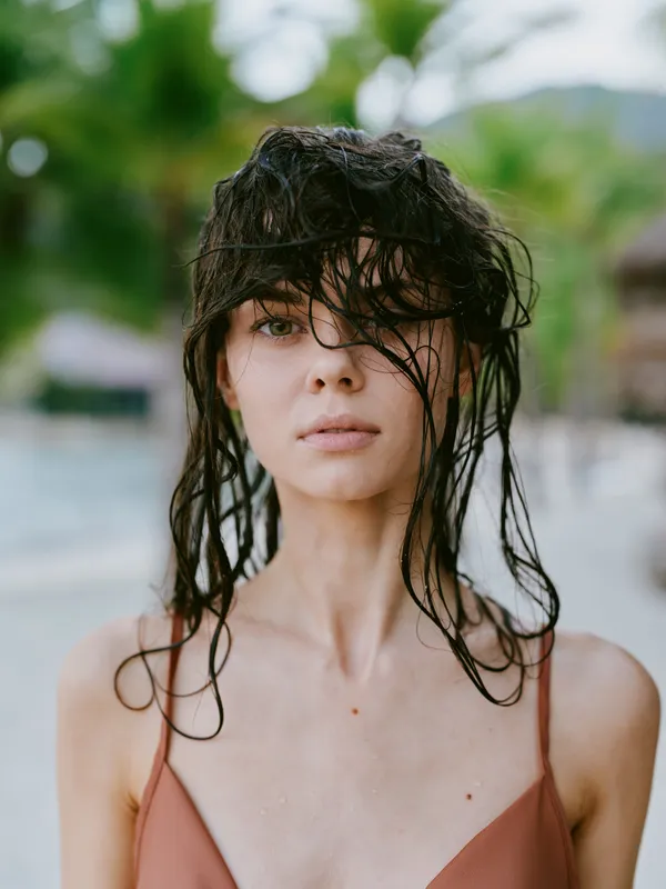 young woman with wet hair standing outdoors in summer, serene expression, natural light, soft background, casual wear