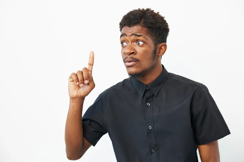 African American man with a thoughtful expression, raising his finger in a gesture, showcasing inspiration and creativity in a studio setting.