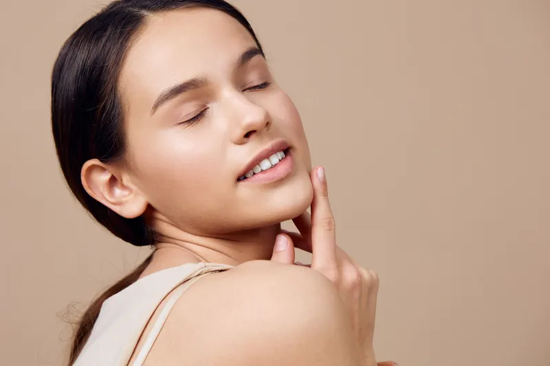 A serene young woman with closed eyes showcasing natural beauty and glowing skin against a soft beige background, radiating calmness and confidence