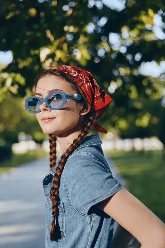 Modern boho-western denim street style woman wearing blue sunglasses and red bandana under natural sunlight in a casual lifestyle outdoor setting with vibrant film color.