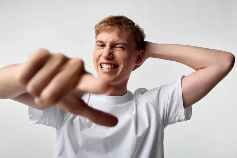 Hands forming a strong thumbs down gesture, a young man wearing a white t shirt shows disapproval and frustration, expressive facial grimace, casual studio shot conveying rejection and critique