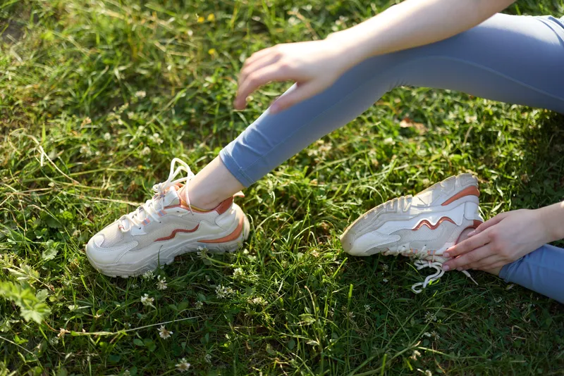 A young woman in stylish athletic shoes sitting on green grass, showcasing relaxation and outdoor activity, perfect for spring fitness or lifestyle themes
